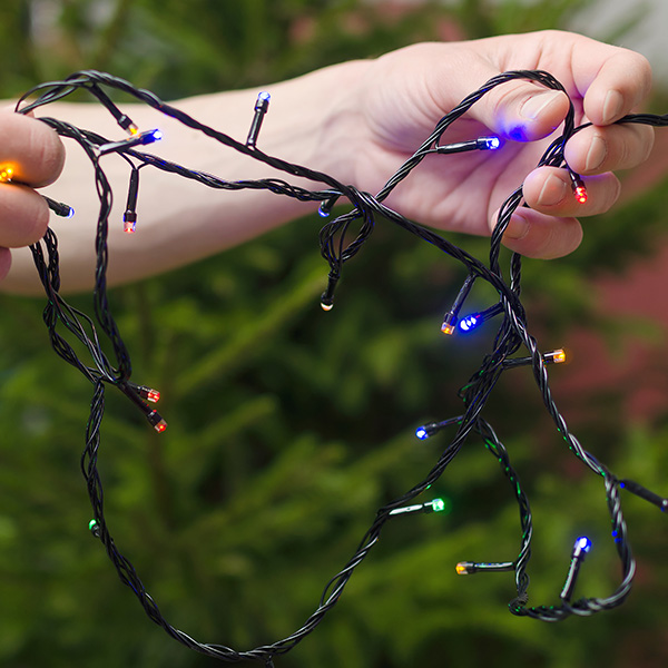 Christmas lights in the male hands on a Christmas fir tree backg
