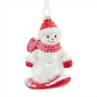 Snowman ornament wearing a red hat and scarf, hanging by a ribbon against a white background
