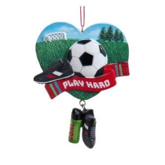 Heart-shaped ornament with a soccer ball, black shoe, and a red ribbon reading 'PLAY HARD' over a grassy field backdrop.